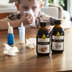 Chłopiec z katarem sięga po olej z czarnuszki, szukając domowych sposobów na uczulenie skórne. Na stole stoją butelki oleju i spray do nosa.
