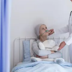 Dziewczynka z rakiem serca w szpitalnym łóżku, z tlenem i pluszowym misiem, otrzymuje wsparcie od lekarki.
