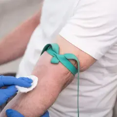 Przygotowanie do pobrania krwi na badanie HBs. Ręka pacjenta z opaską uciskową, pielęgniarka dezynfekuje skórę.