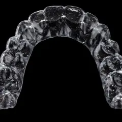 Przezroczysty aparat Invisalign, trzymany palcami, z widocznymi wypustkami dopasowanymi do zębów.