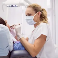 Dentystka w masce i rękawiczkach wykonuje zabieg, kiedy leczenie kanałowe jest konieczne.