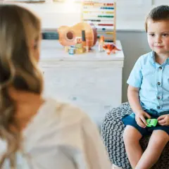 Chłopiec w niebieskiej koszuli siedzi na pufie, rozmawiając z psychologiem.