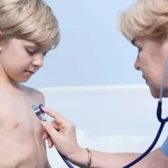 Lekarz osłuchuje klatkę piersiową chłopca, diagnozując zapalenie oskrzeli bez gorączki.