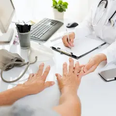 Lekarz bada dłonie pacjentki, oceniając objawy mogące wskazywać na odczyn Waalera-Rosego.