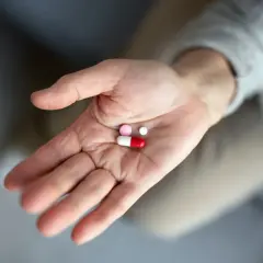 Dłoń trzyma kilka tabletek, w tym czerwonobiałą kapsułkę, która może być antybiotykiem na zęba.