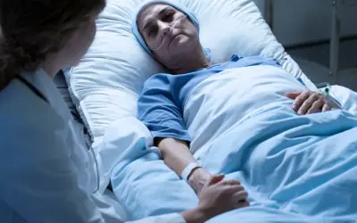 Kobieta w szpitalnym łóżku, z rurką tlenową, doświadcza kacheksji nowotworowej. Lekarka trzyma ją za rękę, okazując wsparcie.