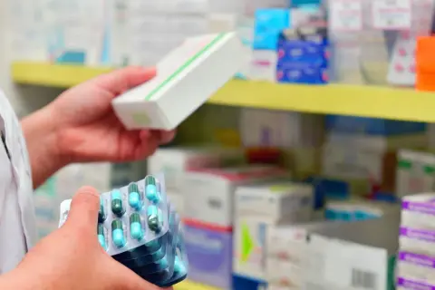 Farmaceuta trzyma opakowanie leku i kilka blistrów z kapsułkami. Ważna recepta na antybiotyk jest kluczowa.