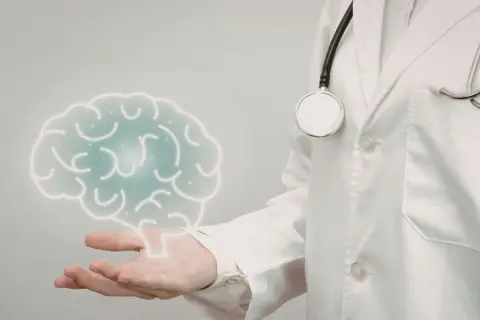 Lekarz w białej kitle z latarką i stetoskopem prezentuje symboliczny mózg, sugerując badanie neurologiczne.