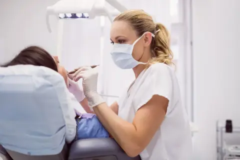 Dentystka w masce i rękawiczkach wykonuje zabieg, kiedy leczenie kanałowe jest konieczne.