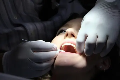 Uśmiechnięta pacjentka u dentysty, który używa narzędzi i pasty devipasta do wybielania zębów.
