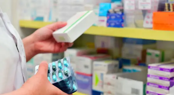 Farmaceuta trzyma opakowanie leku i kilka blistrów z kapsułkami. Ważna recepta na antybiotyk jest kluczowa.