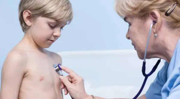 Lekarz osłuchuje klatkę piersiową chłopca, diagnozując zapalenie oskrzeli bez gorączki.