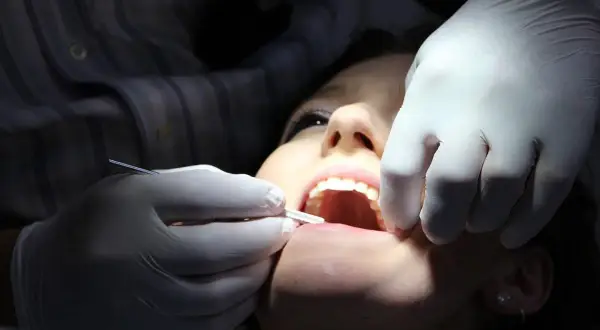Uśmiechnięta pacjentka u dentysty, który używa narzędzi i pasty devipasta do wybielania zębów.