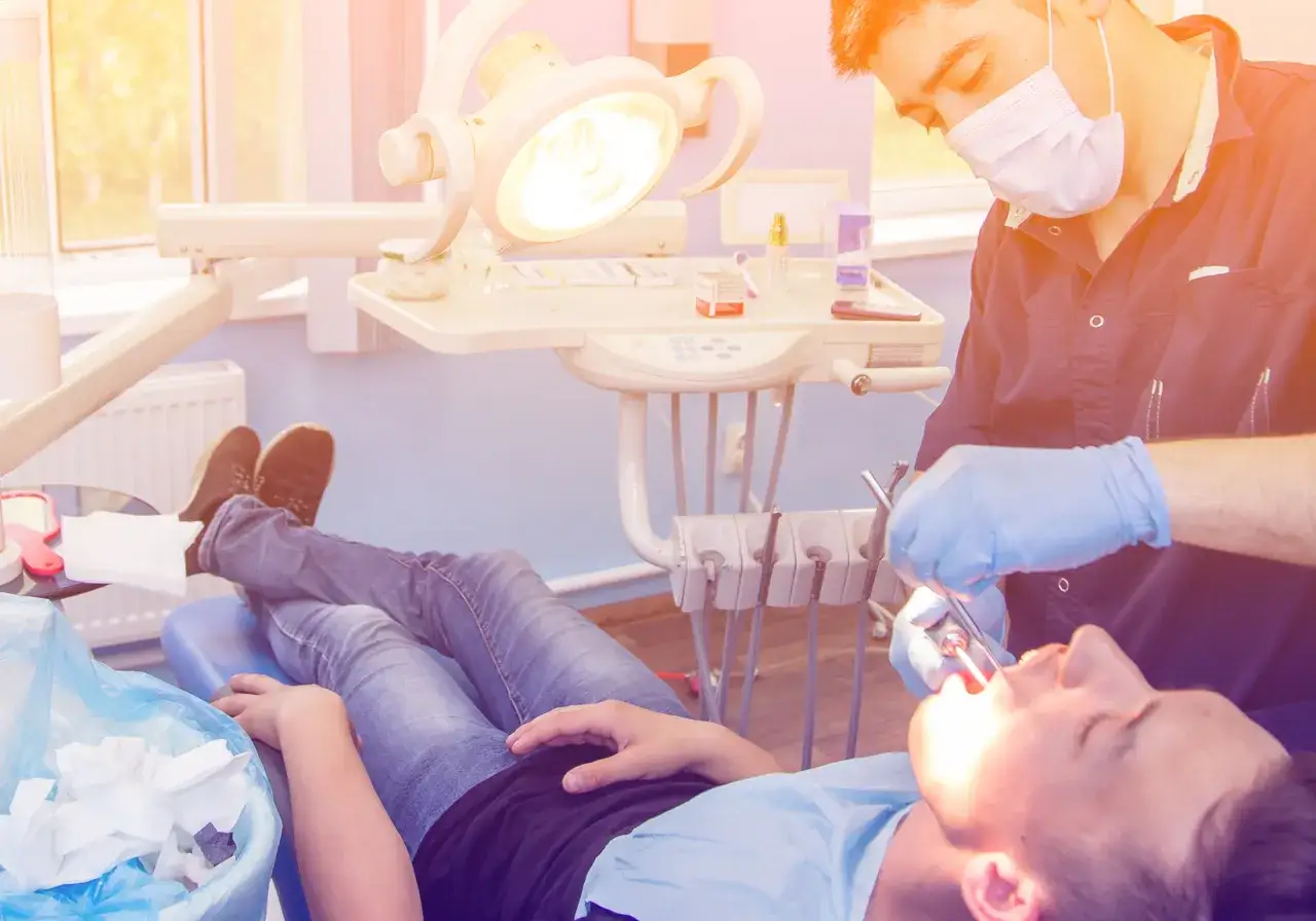 Dentysta w rękawiczkach wykonuje ekstrakcję zęba u pacjenta leżącego na fotelu.
