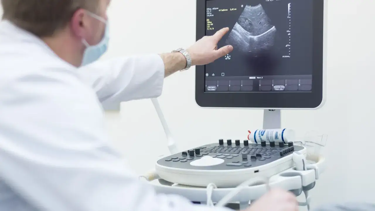 Lekarz wskazuje na ekran aparatu USG, gdzie widoczny jest obraz narządu. Przygotowanie do biopsji cienkoigłowej.