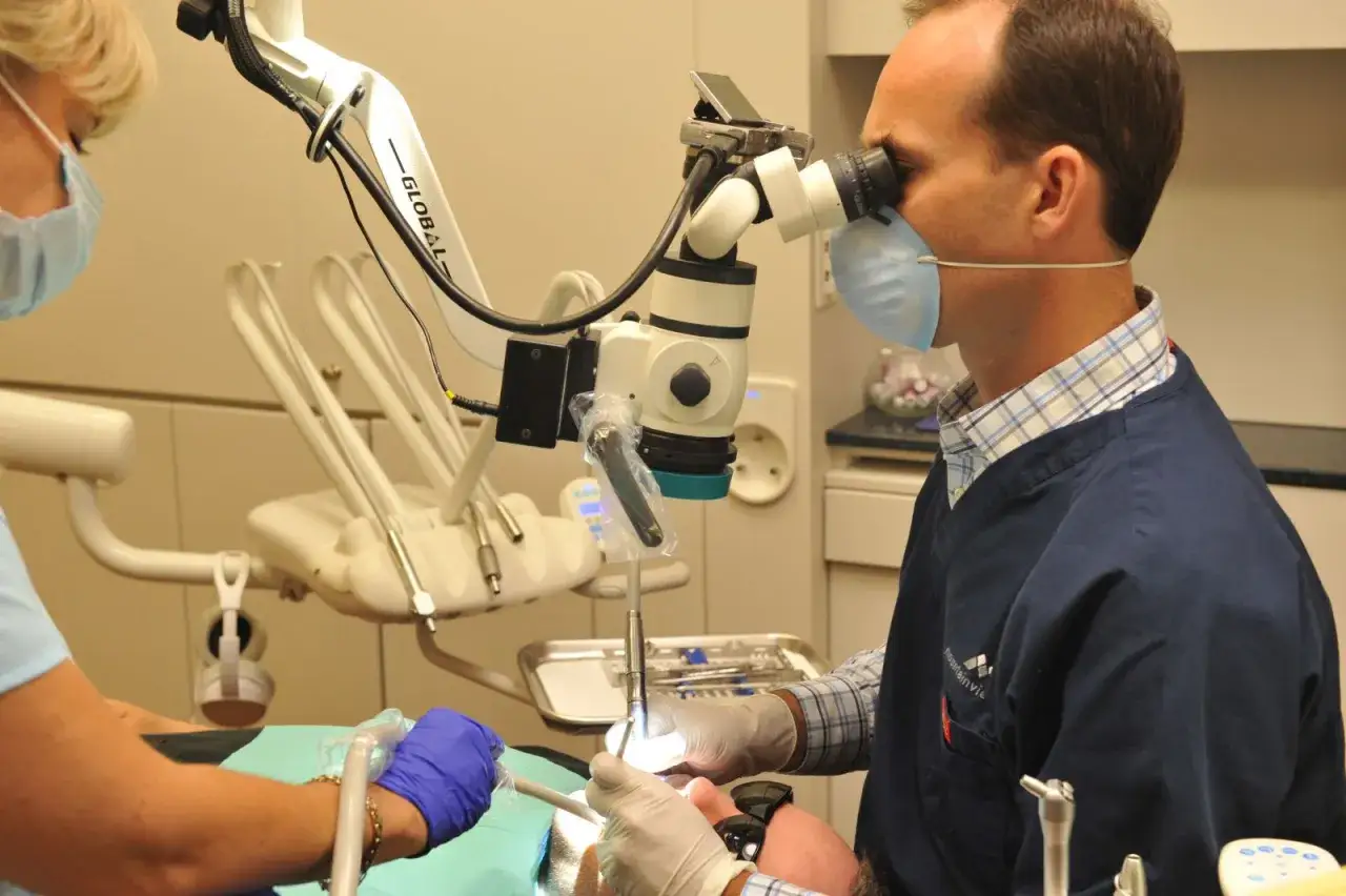 Dentysta wykonuje leczenie kanałowe pod mikroskopem, precyzyjnie pracując z narzędziami.