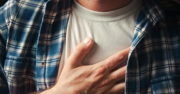 Dłoń na piersi, odczuwając niepokojący ucisk w klatce piersiowej. Mężczyzna w koszuli w kratę.