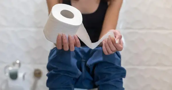 Osoba siedząca na toalecie trzymająca rolkę papieru toaletowego, sugerująca problemy z biegunką.