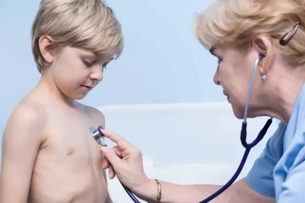 Lekarz osłuchuje klatkę piersiową chłopca, diagnozując zapalenie oskrzeli bez gorączki.